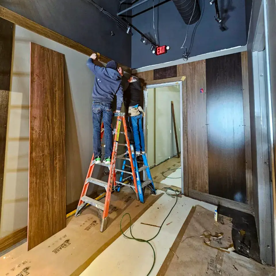 Handymen installing wood paneling on interior walls during renovation